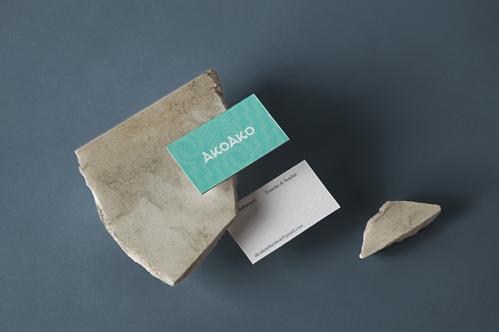 An image featuring two business cards for Akoako lying on a sandy-coloured rock. The cards feature a Maori pattern as the background, with the Akoako logo centred on each card. The use of the Maori pattern adds a sense of cultural significance and uniqueness to the design, while the sandy-coloured rock adds a natural and organic element to the overall composition. The image serves as a visual representation of the brand's aesthetic.