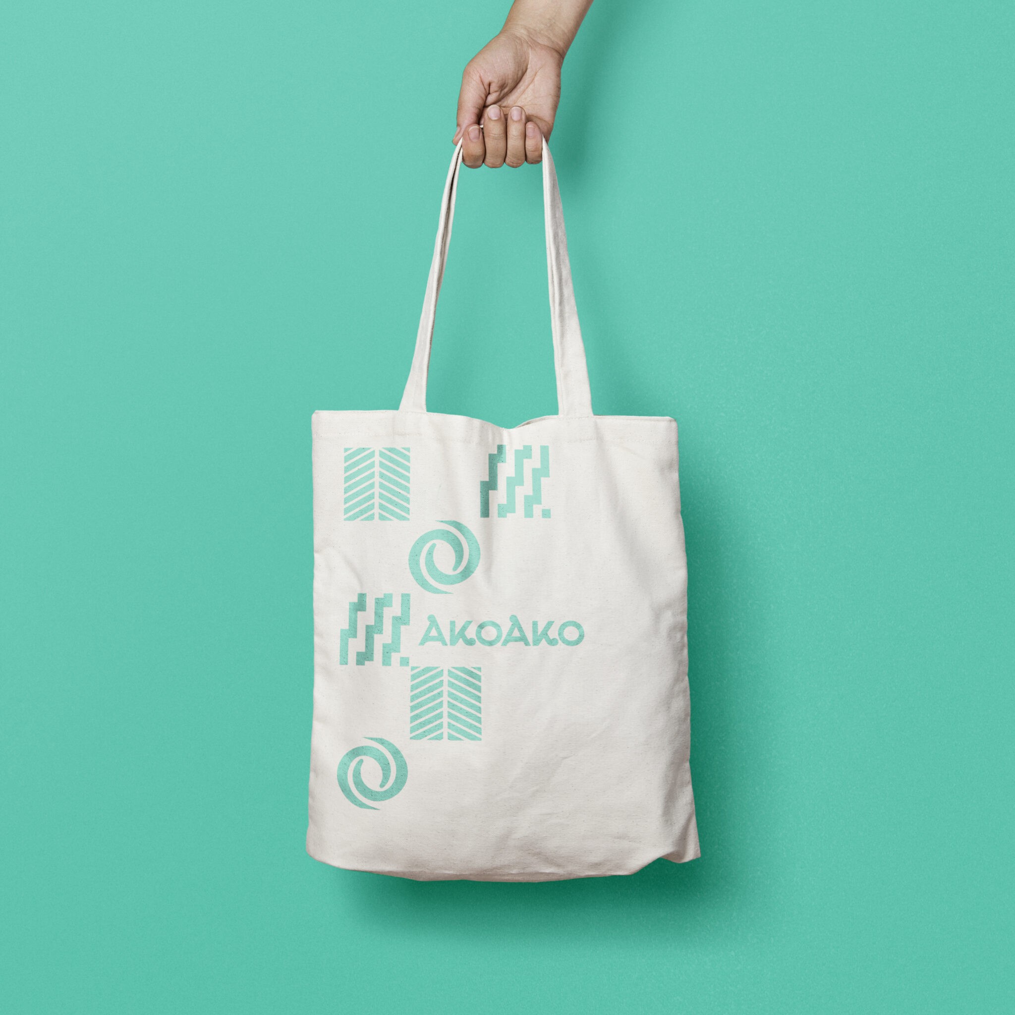 A mockup of a tote bag with a teal background featuring a branding with a Maori pattern. The pattern consists of a series of teal-coloured shapes and features the brand’s name AkoAko.