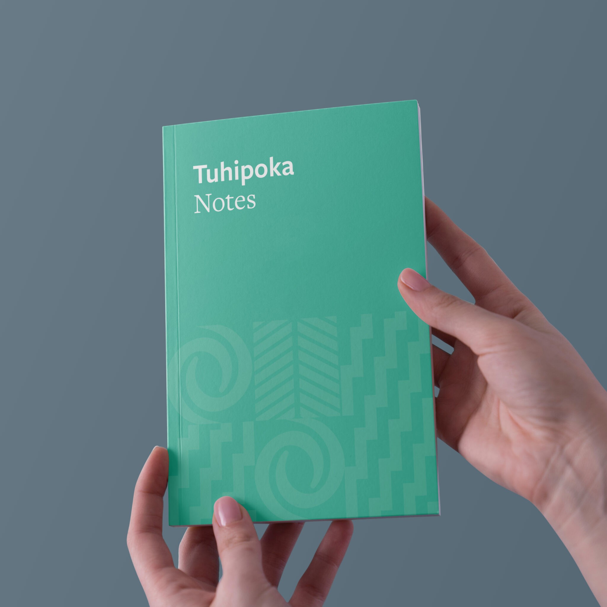 Notebook designed in Akoako Branding held by two hands and saying "Tuhipoka"