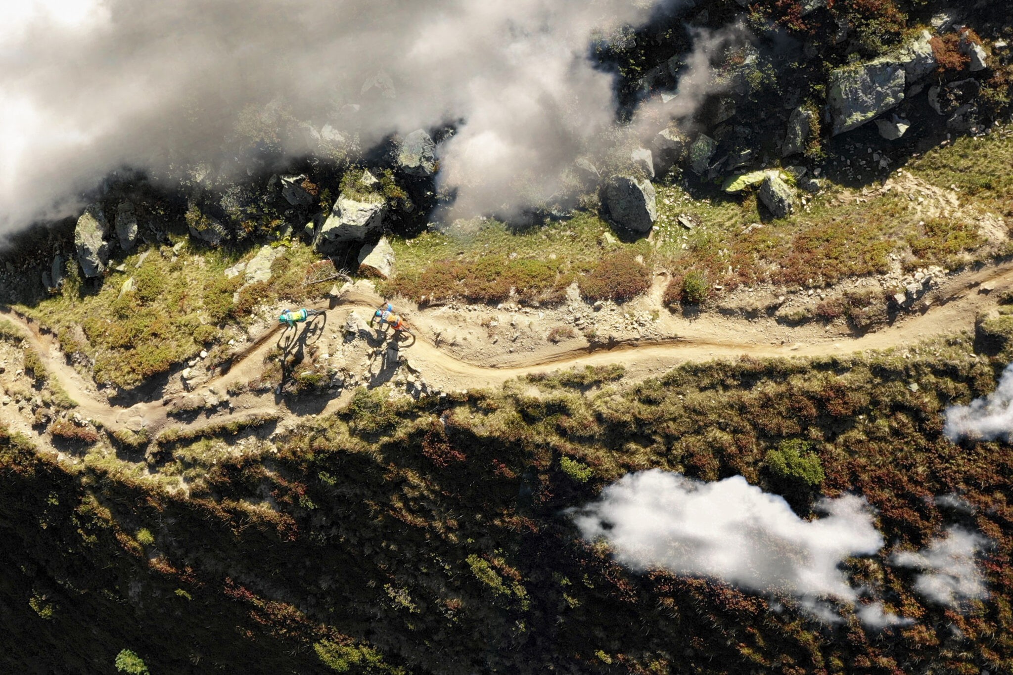 A birds-eye view image of mountain bikers riding a trail amidst a bushy landscape.