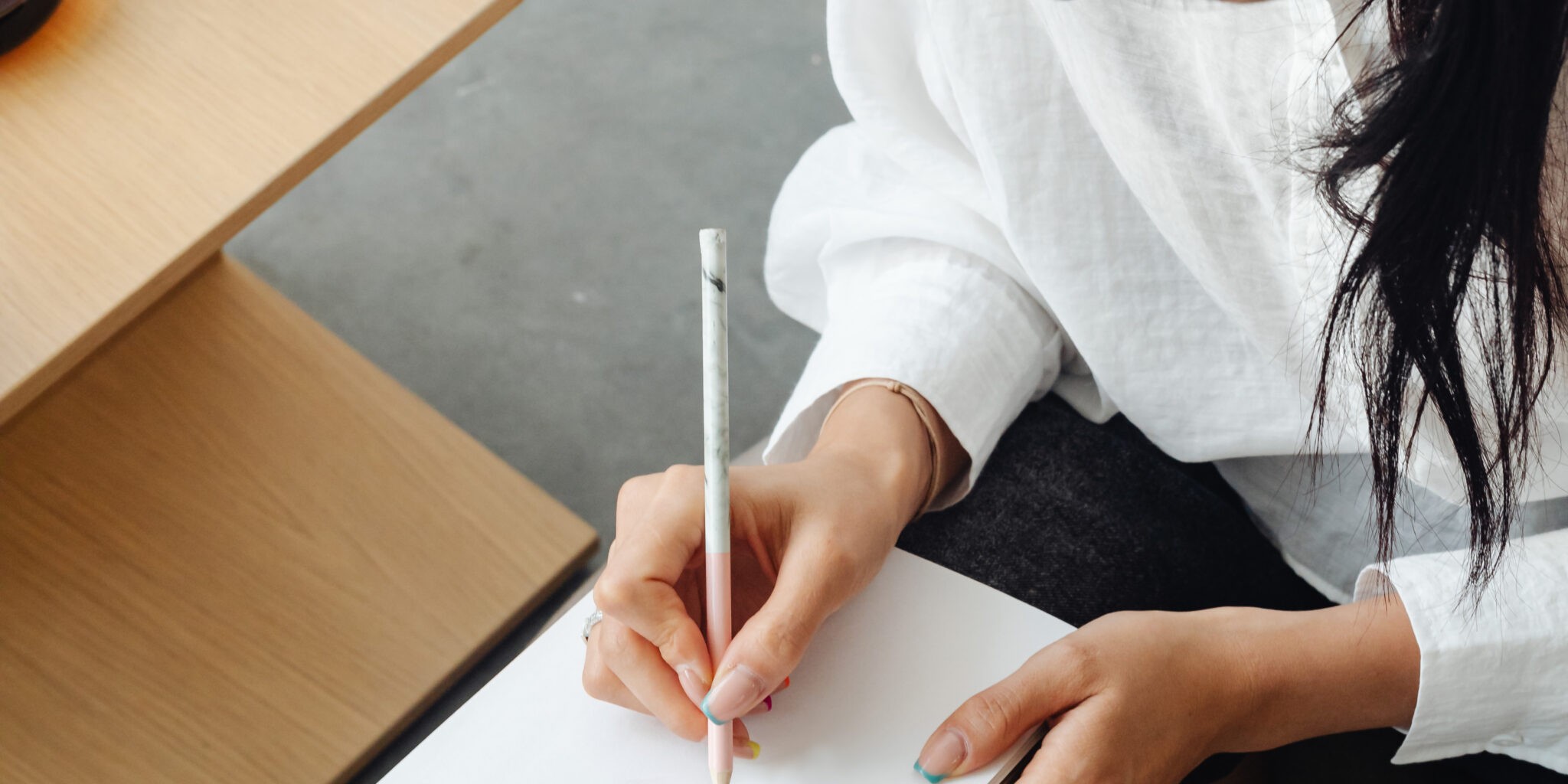 A woman sits with a pen in hand, poised above a blank notebook. The focus is on her hand and the notebook. The image is symbolic of the topic of brand voice, representing the blank canvas one faces when starting to develop their brand voice.