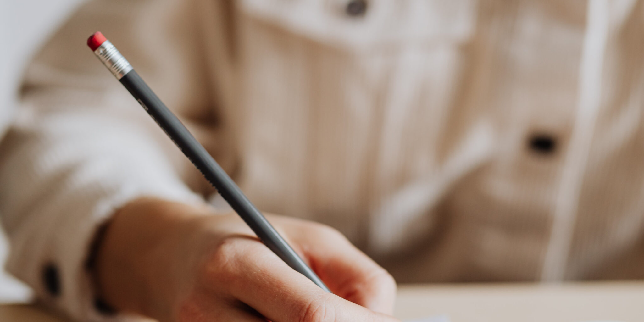 Image of a woman’s hand holding a pencil and writing, symbolising the act of writing a tagline. This image introduces the blog post titled "What is a Tagline and How to Write One That Sticks."