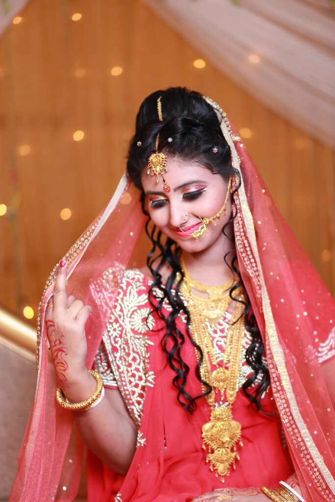 Das Bild zeigt eine indische Braut, die ein rotes Hochzeitskleid mit aufwändigen Goldverzierungen und Schmuckstücken trägt. Rot ist in der indischen Kultur eine traditionelle Farbe für Bräute und symbolisiert Glück, Reinheit und Wohlstand. Das Bild ist ein Beispiel dafür, wie unterschiedlich die Farbwahrnehmung in verschiedenen Kulturen und Traditionen sein kann.