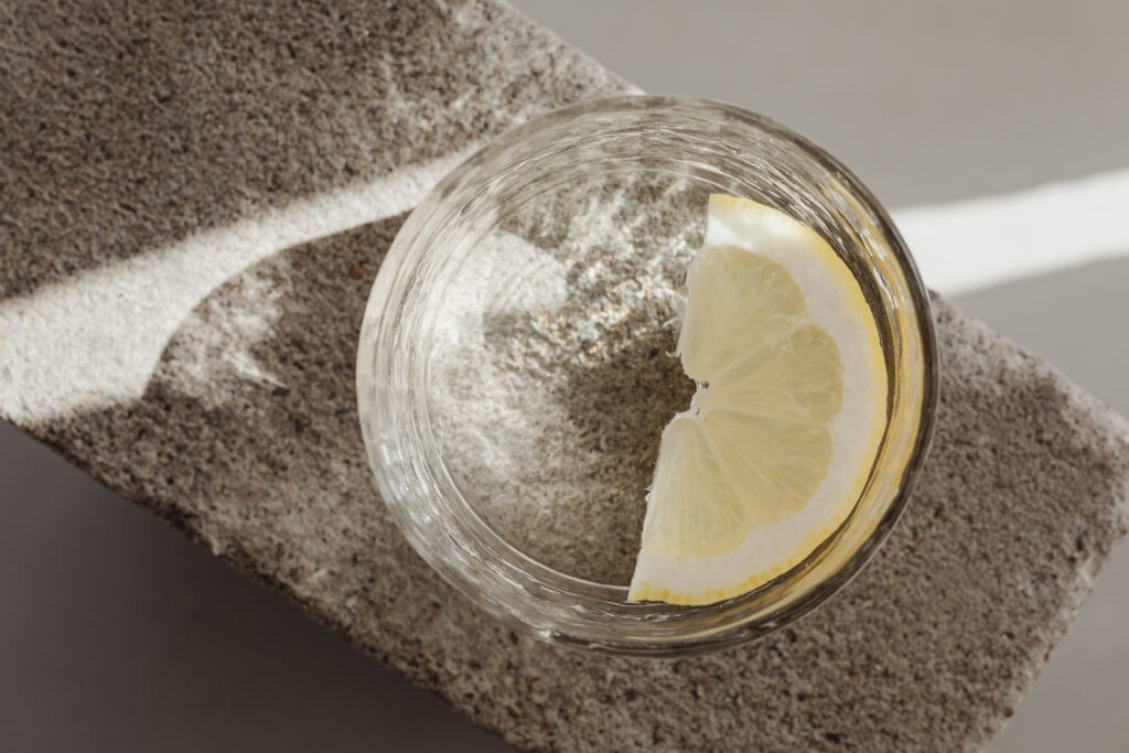 Top view of an unbranded glass of water with a lemon slice on a stone-textured surface against a light curtain background, conveying a brand-free, refreshing, and elegant vibe, as an intro to my article 'A deep dive into branding'