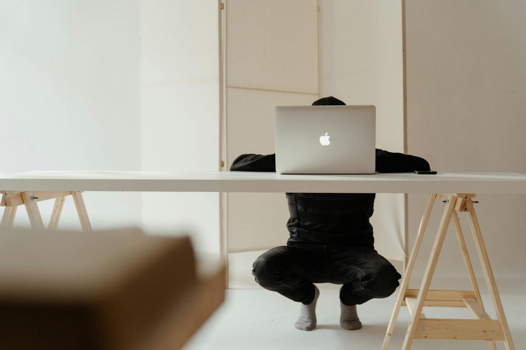 A man crouching behind a desk on a laptop as the intro image for the blog article "15 Reasons Why Your Brand Still Needs a Website in 2025"