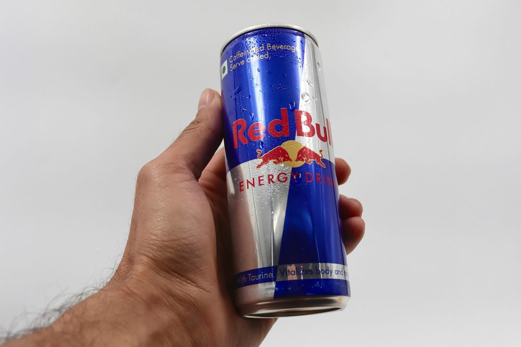 Hand holding Red Bull can that is easily recognisable by its blue and silver slanted rectangles.