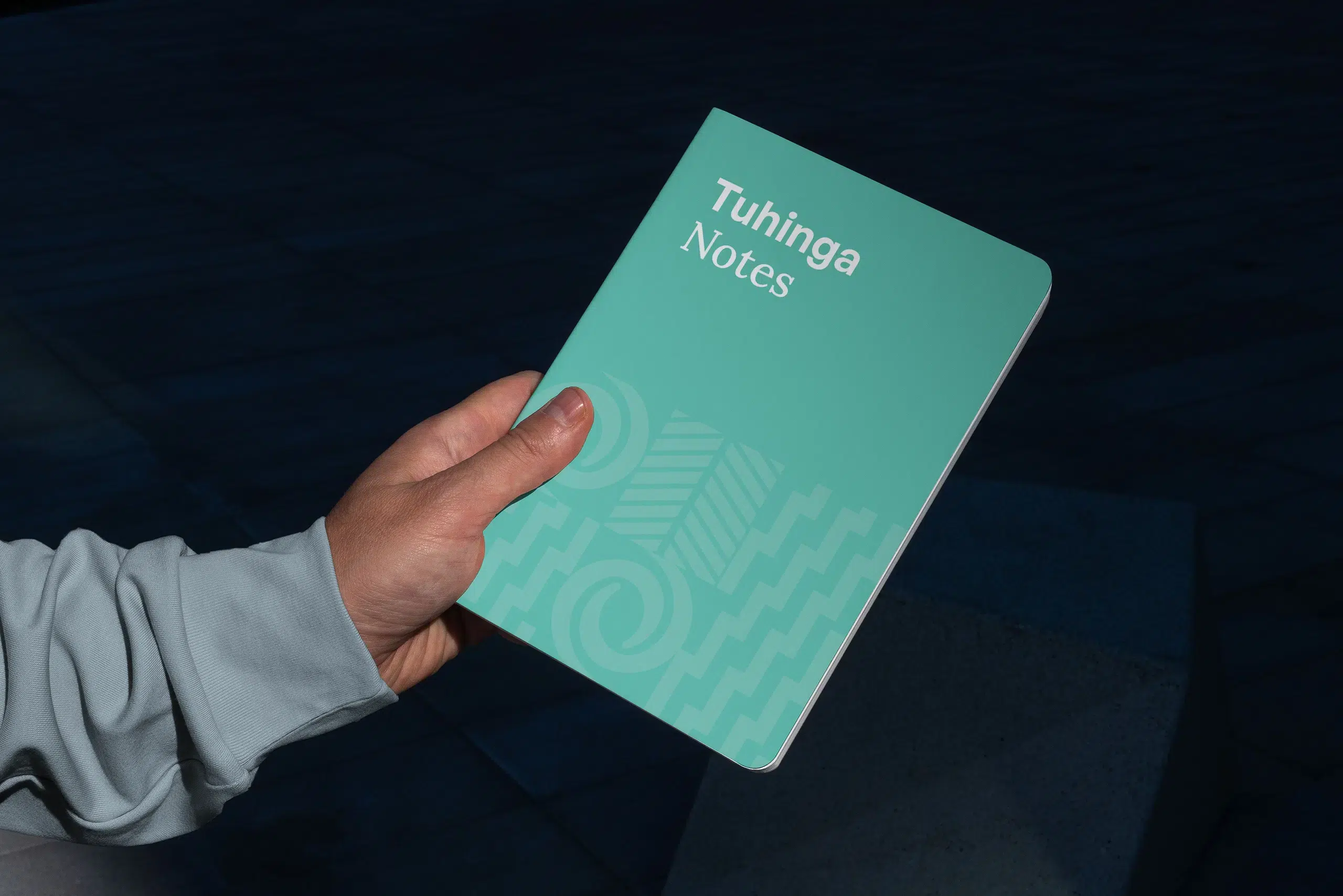 Eine Hand, die ein Notizbuch hält, das das Corporate Design für Akoako, ein te reo Māori Ausbilder, illustriert.