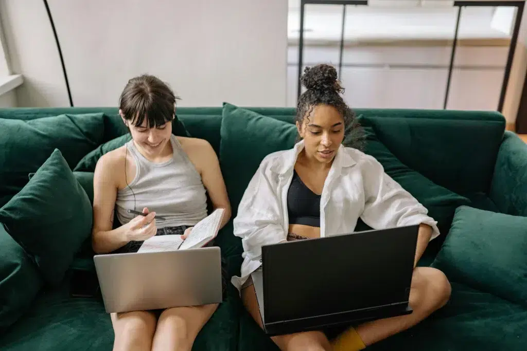Zwei Frauen sitzen auf einem Sofa, schauen auf ihre Laptops und führen einen Brand-Audit durch.
