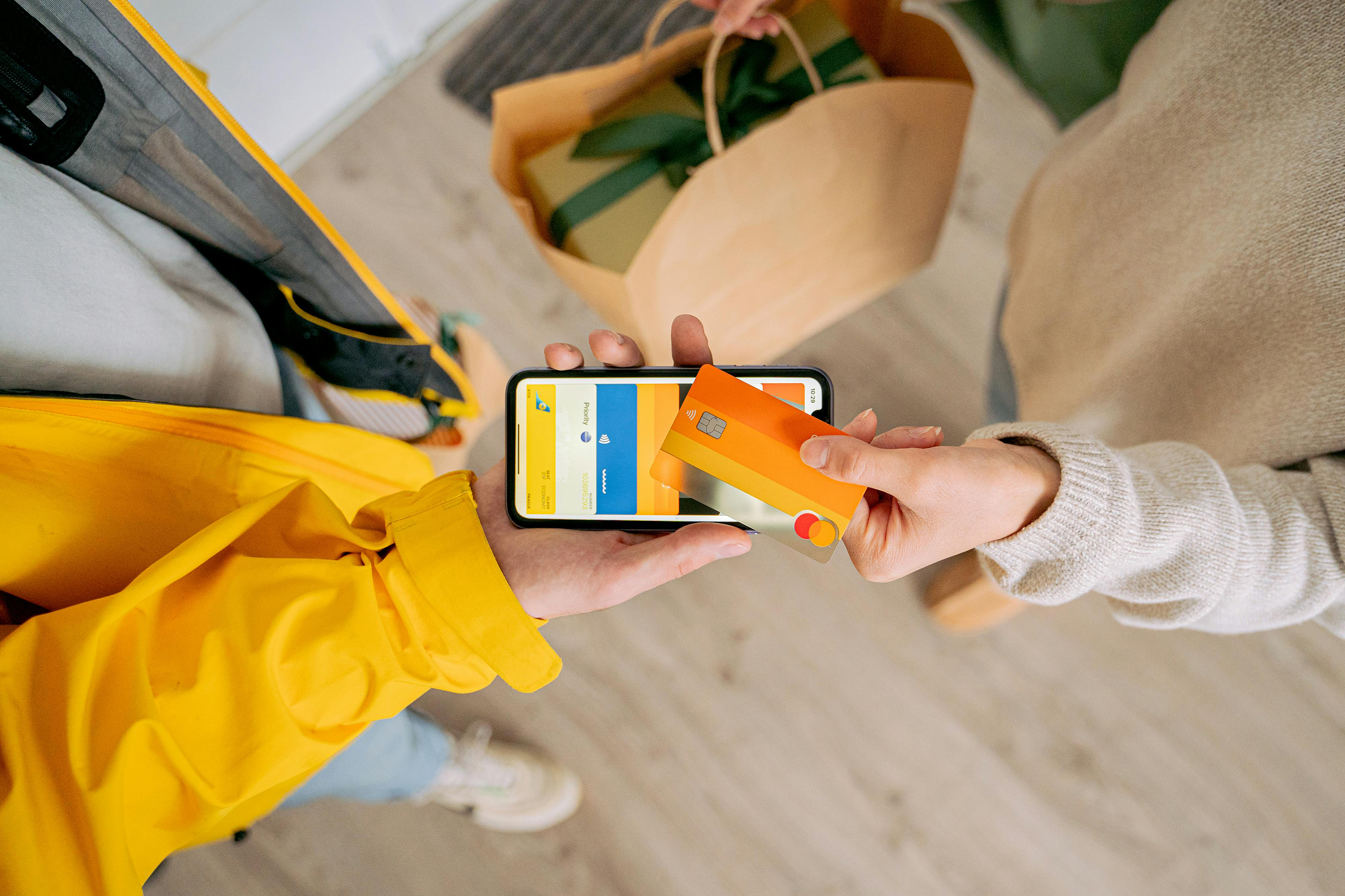 Hands of two people interacting with a mobile phone, credit card, and paper bag—representing everyday brand touchpoints in a digital and physical context.