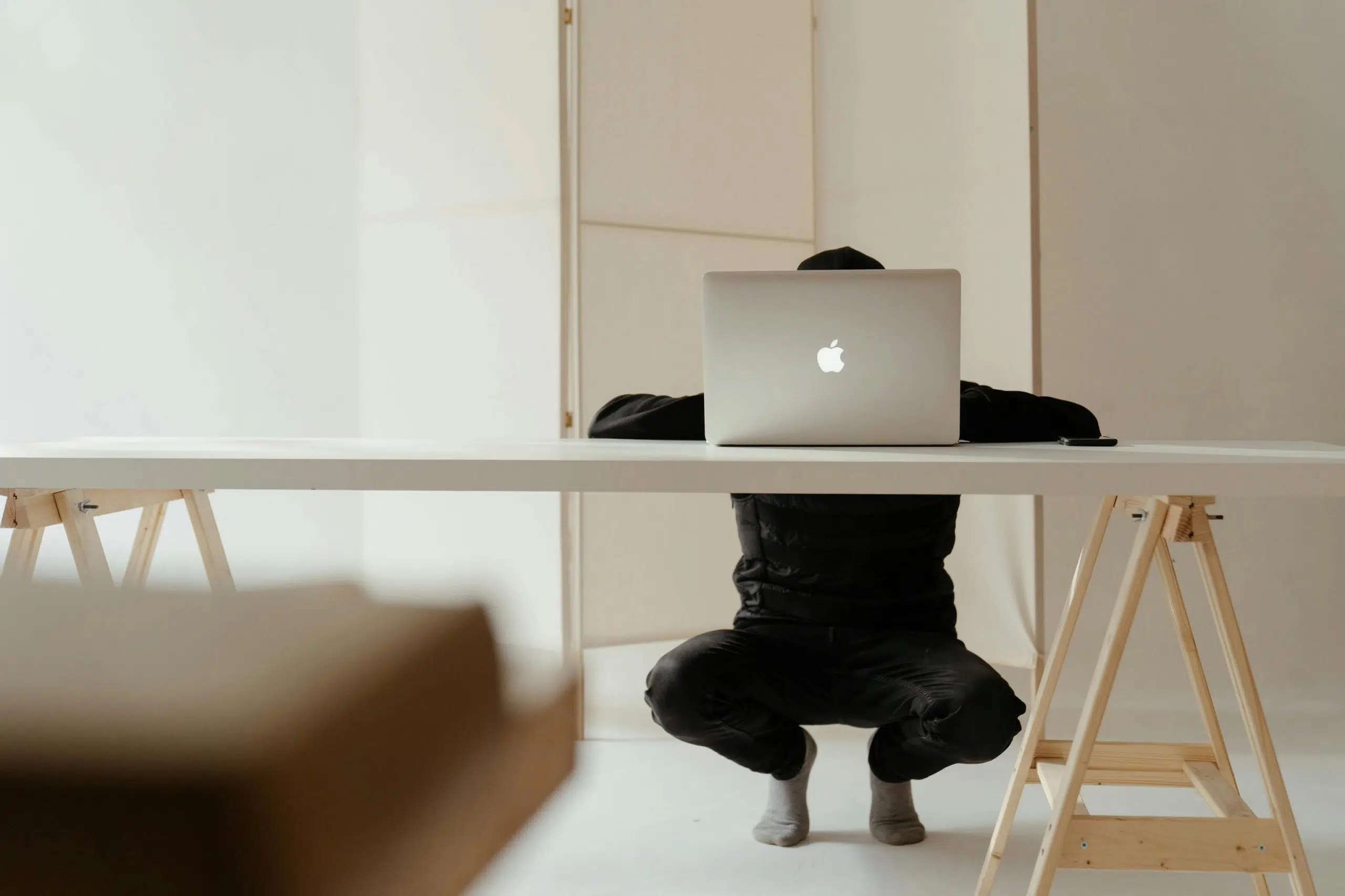 A man crouching behind a desk on a laptop as the intro image for the blog article "15 Reasons Why Your Brand Still Needs a Website in 2025"