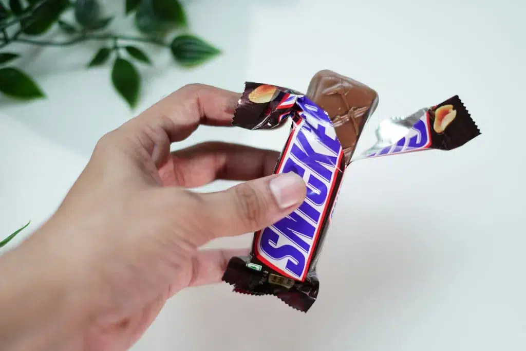 Die Snickers-Verpackung zeigt einen braunen Hintergrund mit fetter blauer Schrift auf einem weißen Panel, das rot umrandet ist – und ist dadurch auch ohne den Markennamen sofort wiedererkennbar.