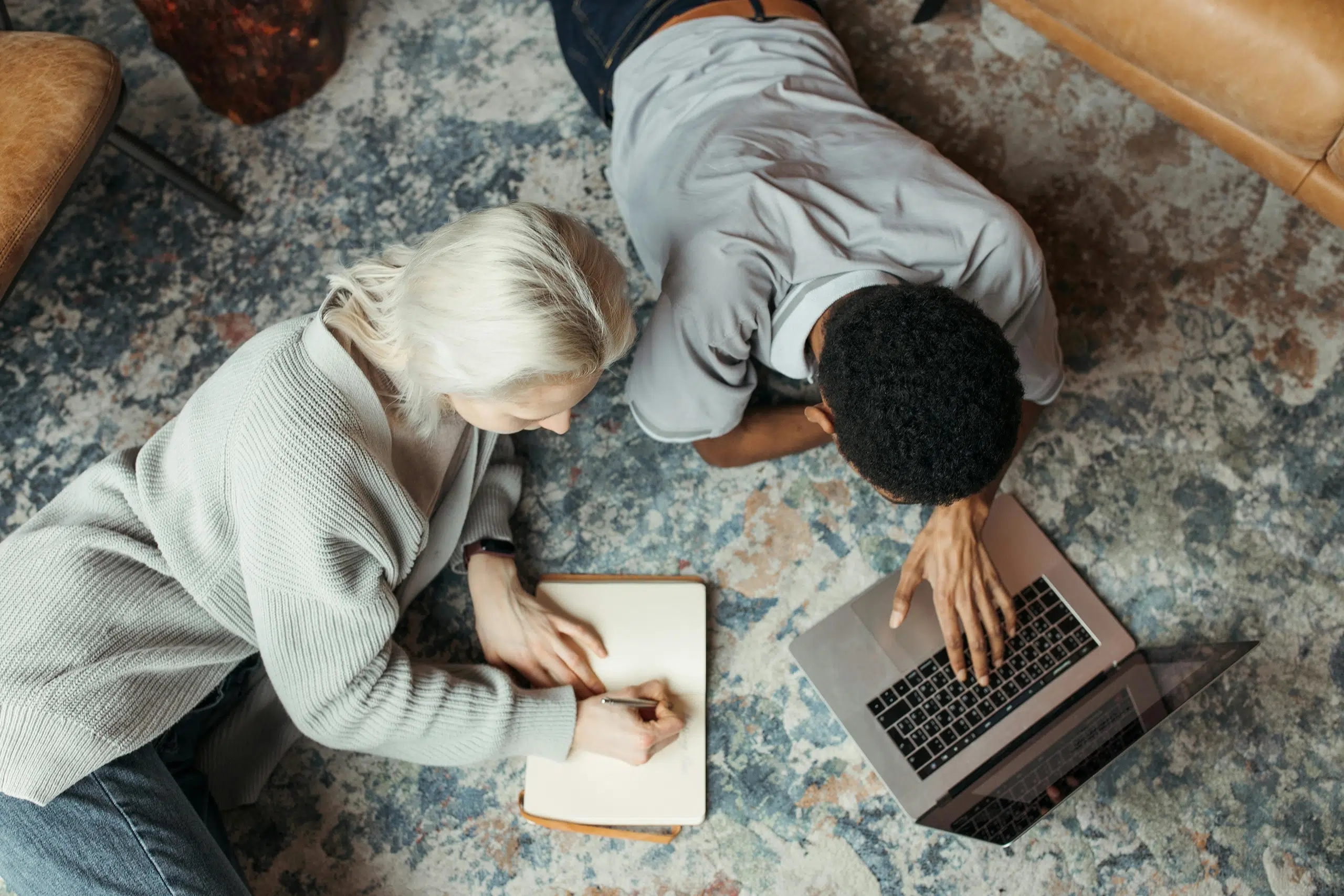 Two people lying on the floor working over a laptop and notebook. This is an introduction to an article on tips to design a business website that converts.