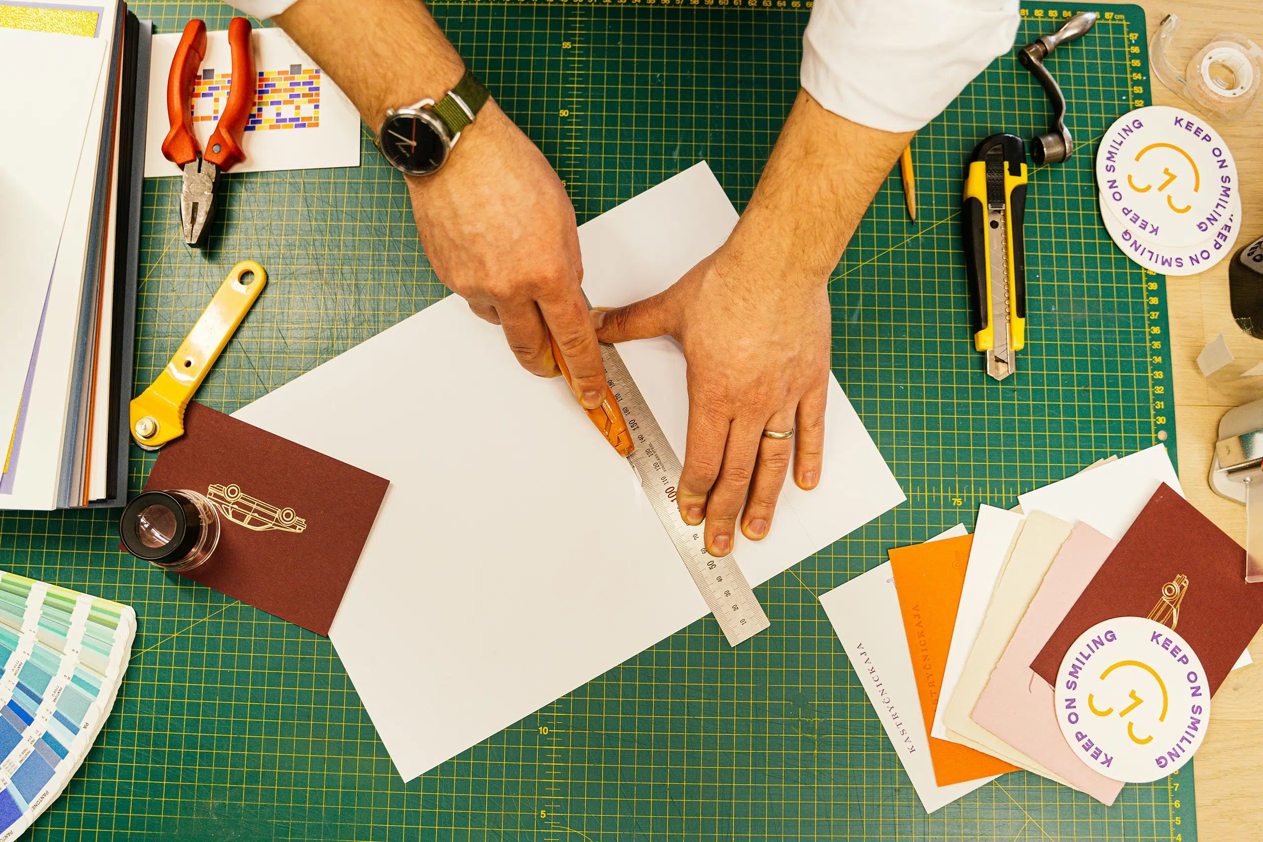 Hands working on a cutting mat surrounded by branding tools—the visual representation for an article on the best branding tools for designers and small business owners.