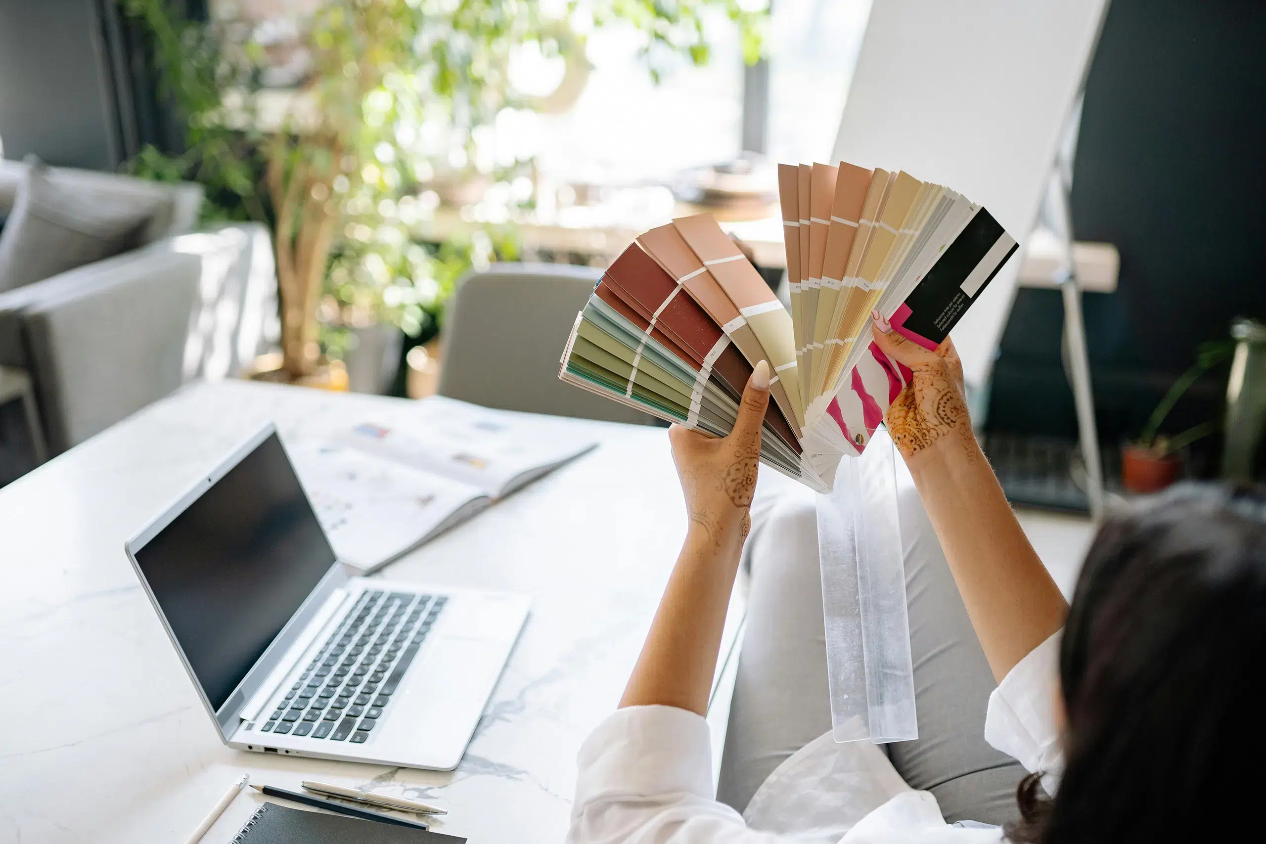 Eine Frau sitzt an einem Schreibtisch, betrachtet einen Pantone-Farbfächer und fragt sich: Wie viele Farben sollte eine Marke haben?