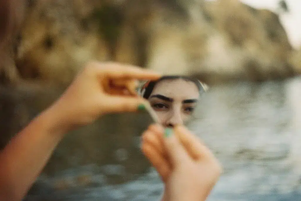 Eine Person, die einen Teil ihres Gesichts in einem zerbrochenen Spiegel erblickt—Symbolhaft für eine fragmentierte Identität und die Suche nach dem, was eine Marke wiedererkennbar macht.