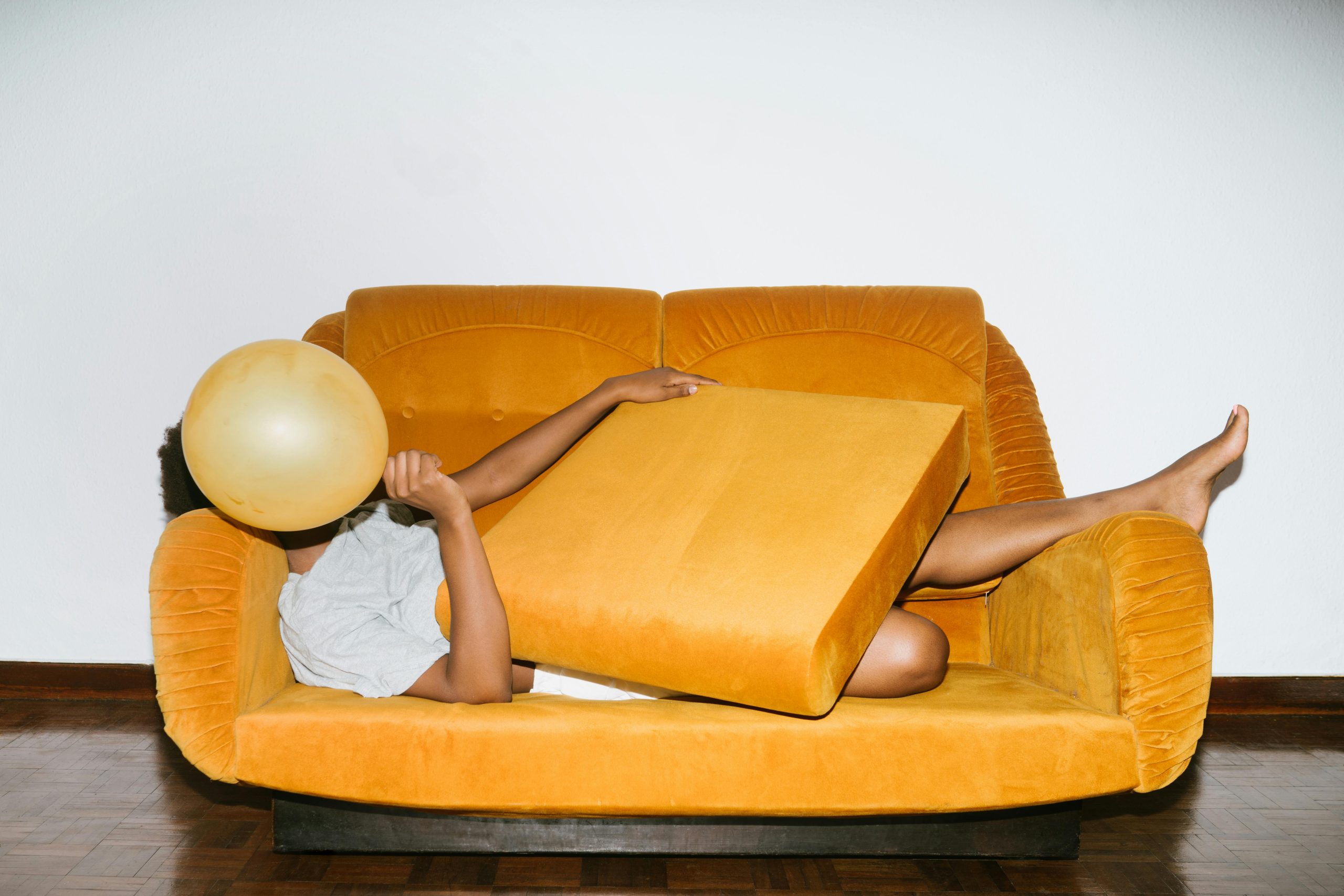 Woman lying playfully on a yellow sofa with cushions, example of a creative image found on one of the best stock photo sites