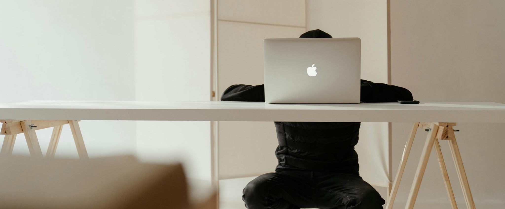 A man crouching behind a desk on a laptop as the intro image for the blog article "15 Reasons Why Your Brand Still Needs a Website in 2025"