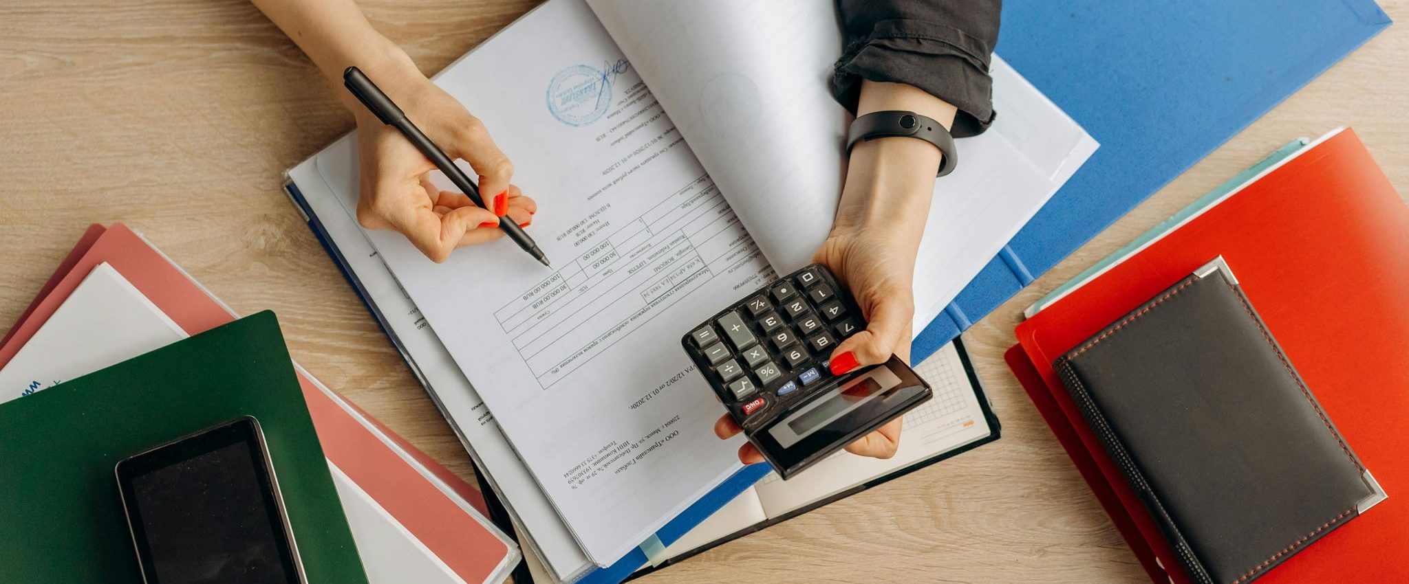A close-up of hands reviewing documents at a desk, with folders and a calculator visible—setting the scene for an article about conducting a brand audit as a small business.